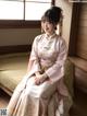 A woman in a pink kimono sitting on a bed.