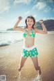 A woman in a bikini jumping in the water on a beach.