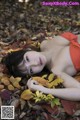 A woman laying on the ground covered in leaves.