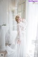 A woman in a white dress standing in front of a window.