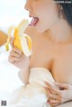 A woman in a white dress eating a banana.