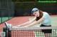 A woman leaning over a tennis net on a tennis court.