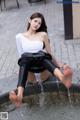 A woman sitting on the edge of a fountain with her feet in the water.