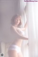 A woman in a white lingerie leaning against a curtain.