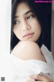 A woman in a white shirt leaning against a wall.