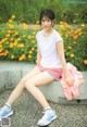 A young woman sitting on a concrete bench in front of flowers.