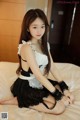 A woman in a maid outfit sitting on a bed.