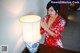 A woman in a red kimono standing next to a lamp.