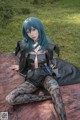 A woman with blue hair sitting on a blanket in the grass.