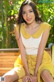 A woman in a yellow dress sitting on a wooden bench.