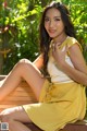 A woman in a yellow dress sitting on a wooden bench.