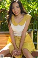 A woman sitting on a wooden bench in a yellow dress.