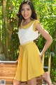 A woman in a yellow skirt posing on a wooden bench.