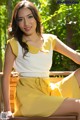 A woman sitting on a wooden bench in a yellow dress.