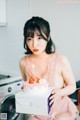 A woman sitting on a washing machine holding a birthday cake.