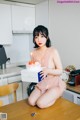 A woman sitting on a kitchen counter holding a birthday cake.