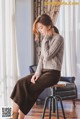 A woman sitting on a stool in front of a window.