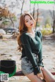 A woman sitting on a bench wearing a green sweater and skirt.