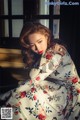 A woman in a floral dress sitting on a window sill.