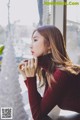 A woman in a red turtle neck sweater leaning against a window.