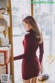 A woman in a red dress standing in front of a window.