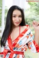 A woman in a red and white robe posing by a window.