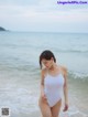 A woman in a white bathing suit standing on the beach.