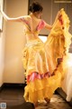 A woman in a yellow and pink dress dancing in a hotel room.