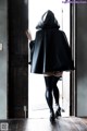 A woman in a black cloak and thigh high boots standing in a doorway.