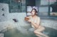 A naked woman sitting in a hot tub holding a bowl of water.