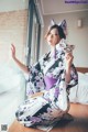 A woman in a kimono sitting on the floor holding a cat mask.