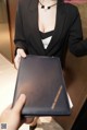 A woman in a black suit holding a black folder.