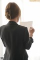 A woman in a black suit writing on a piece of paper.