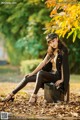 A woman sitting on top of a suitcase in a park.