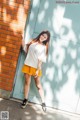 A woman leaning against a brick wall in a yellow skirt.