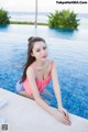 A woman in a pink bathing suit sitting by a swimming pool.