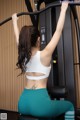 A woman in a white sports bra top and green leggings doing pull ups on a gym machine.