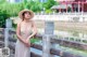 A woman in a dress and hat standing on a bridge.