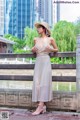 A woman in a white dress and straw hat standing on a bridge.