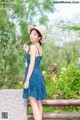 A woman in a blue dress and straw hat posing for a picture.