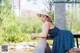 A woman in a blue dress and straw hat sitting on a bench.