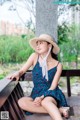 A woman in a blue dress and straw hat sitting on a bench.