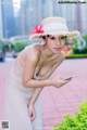 A woman in a white dress and a straw hat holding a cell phone.