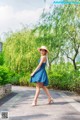 A woman in a blue dress and straw hat walking down a sidewalk.