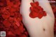 A woman with a tattoo on her stomach surrounded by red rose petals.