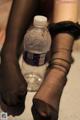 A woman in black stockings holding a bottle of water.