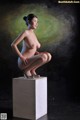 A nude woman sitting on top of a white box.