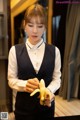 A woman in a black vest holding a banana.