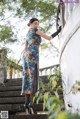 A woman in a blue dress and black gloves leaning against a wall.