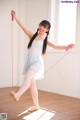 A young girl in a white dress is holding a pink skipping rope.